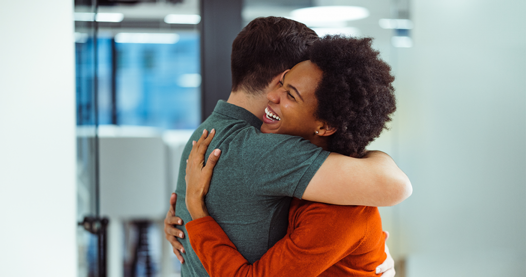 A Black woman is looking joyful as she hugs her white friend after him agreeing to donate sperm