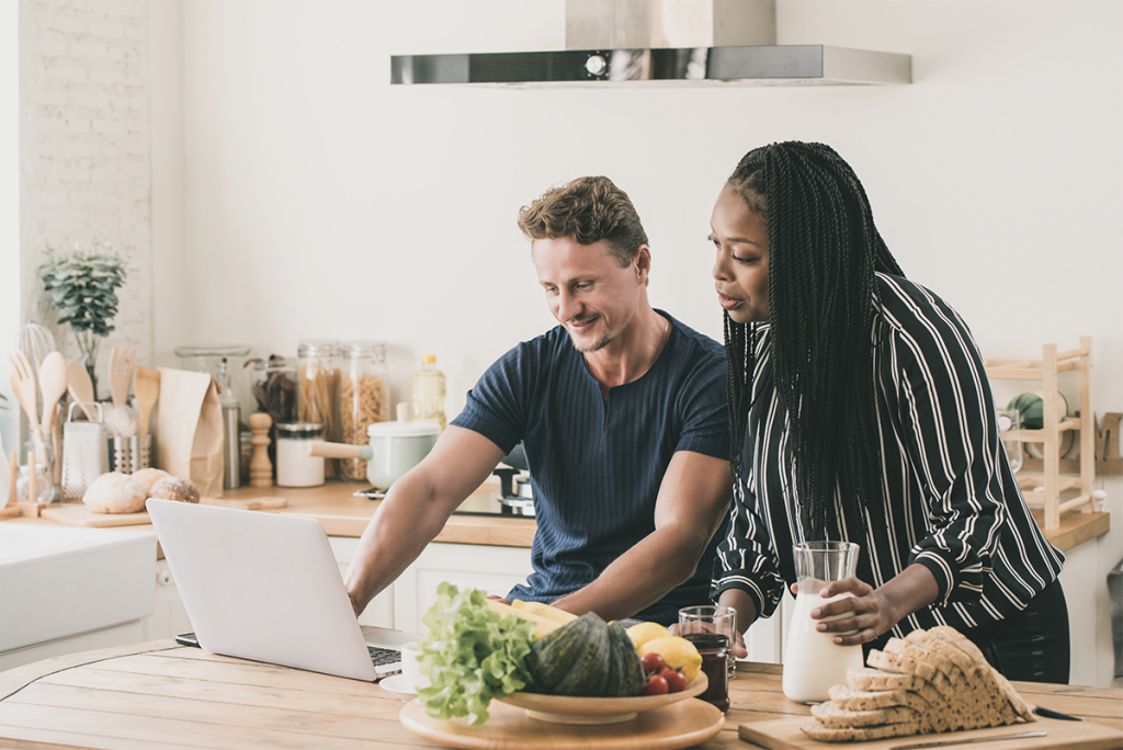 A Black woman and a white male are sat together in a kitchen looking at a laptop about the donation process for known donors